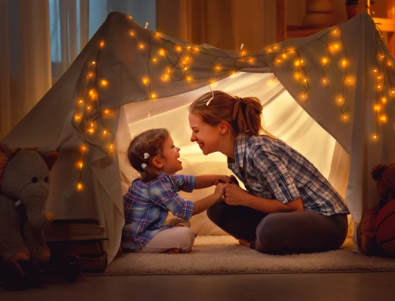 A mother and daughter smiling inside a tent decorated with lights.